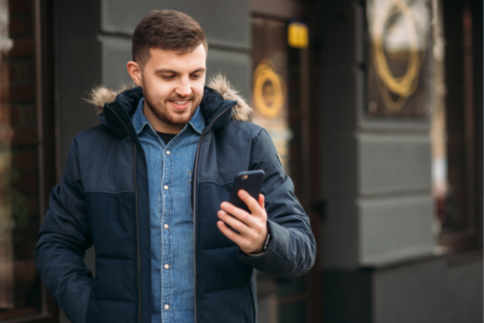 Man walking down the street looking at his phone to check the top 10 affiliate programs earnings for the week.
